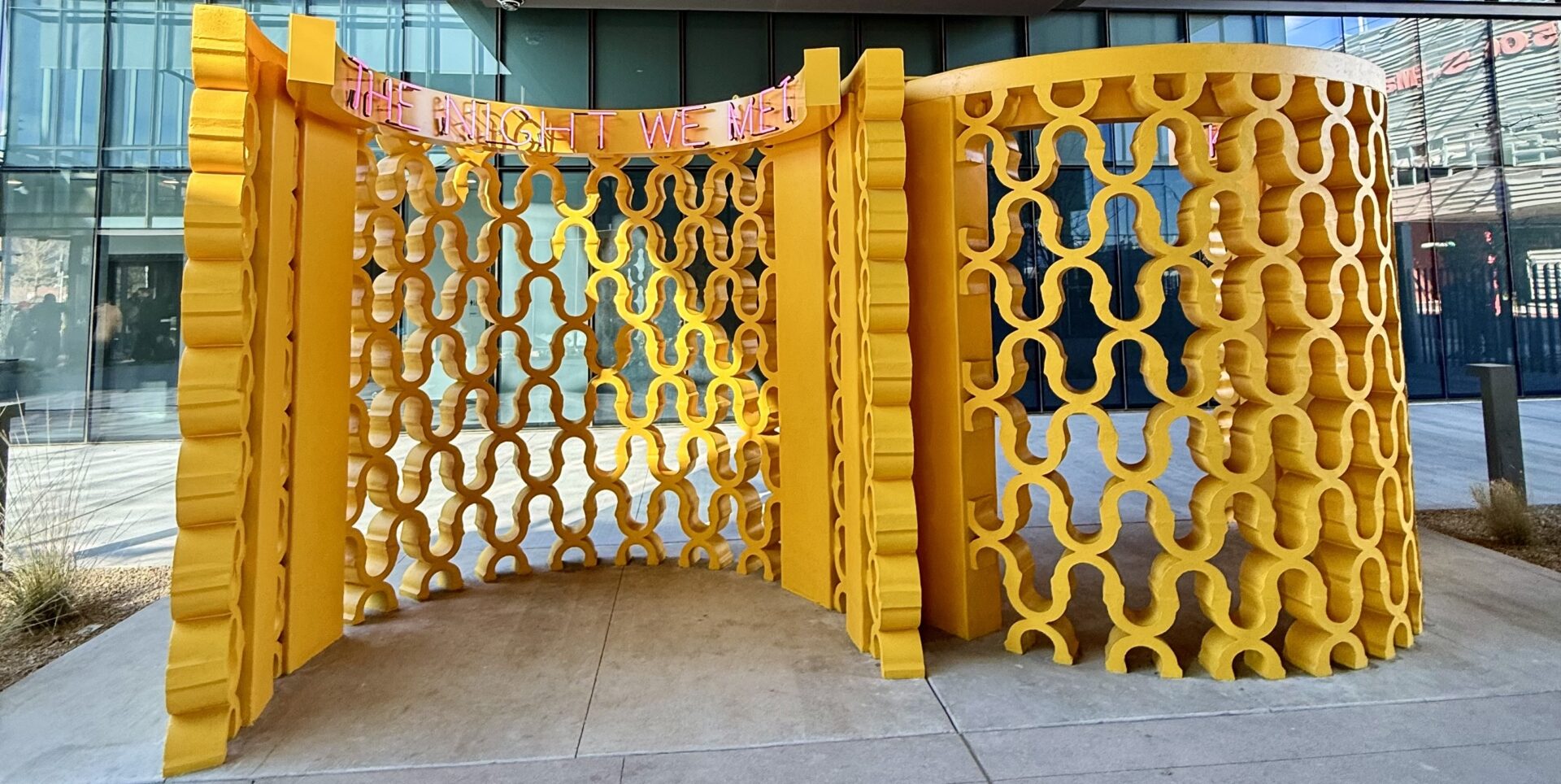 A vibrant yellow mural with interlocking shapes and a banner reading